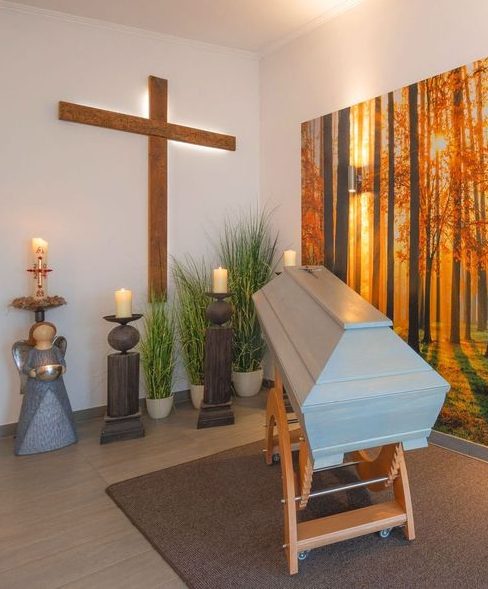 Trauerraum mit Sarg und Holzkreuz an der Wand